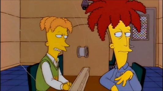 Tahiti Bob, chevelure rouge en palmier et chemise bleue, attablé à côté d'un homme aux cheveux orange bouclés en gilet vert