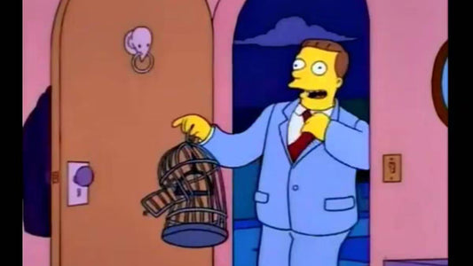 Un homme brun en costume bleu clair et cravate rouge, bouche ouverte, tend une cage à oiseaux vide dans l'embrasure d'une porte
